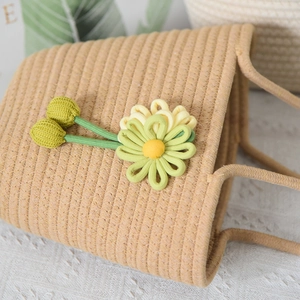 Dettaglio della borsa a mano intrecciata kaki con ciondoli a fiori in tessuto verde e giallo