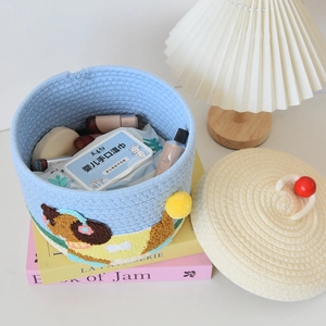 Detail of blue cotton rope woven storage basket with cherry lid and cute cartoon embroidery