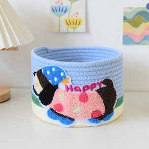 Detail of blue and green woven storage basket with a cute plush cartoon character embroidery