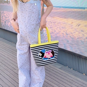 Outdoor shot of a striped knit tote bag with yellow handles and Happy embroidery patch