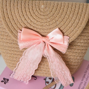 Close-up of woven straw bucket bag featuring a decorative pink satin bow and lace details