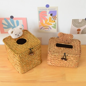 Detail of hand-woven straw tissue box with cute plush bear ornament on wooden desk