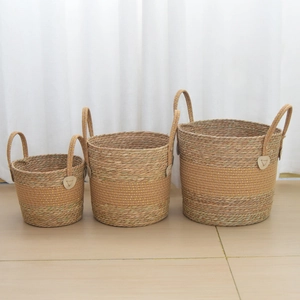 Three-piece set of woven seagrass plant baskets with gold trim and leather accents