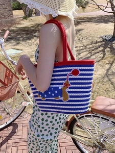 Close-up of woven striped tote bag with cute dog embroidery and red handle detail