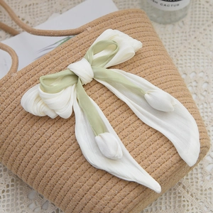 Detailed macro view of woven straw bag with large fabric bow and tulip tassel