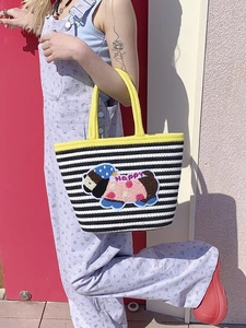 Detail of woven striped tote bag with yellow handle and cute cartoon dog plush patch
