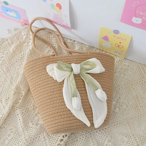 Detail of handmade woven straw bag with white chiffon bow and tulip charms on lace