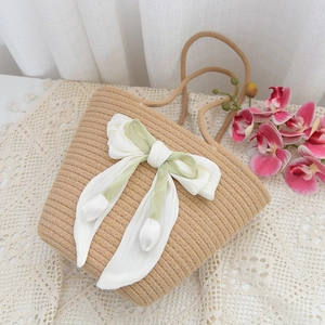 Close-up of woven straw handbag with a large white and green bow and tulip details