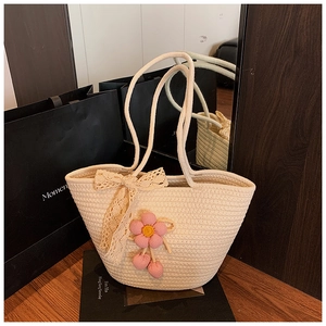 Detail of woven straw tote bag featuring white lace bow and pink cherry floral charms