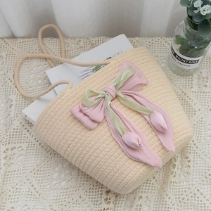 Detail of handmade woven straw bag with a large pink and green satin bow on white lace
