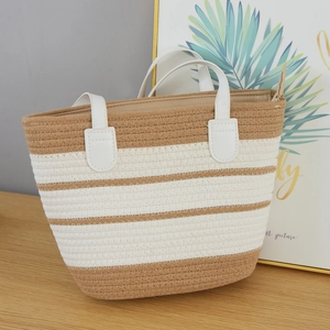 Detail of hand-woven striped tote bag with white leather handles on wooden surface