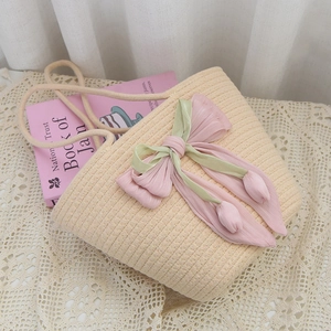 Detail of handmade beige straw bag with pink tulip bow on a white lace tablecloth
