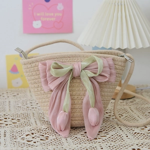 Detail of beige woven straw bucket bag with large pink satin bow and tulip tassels