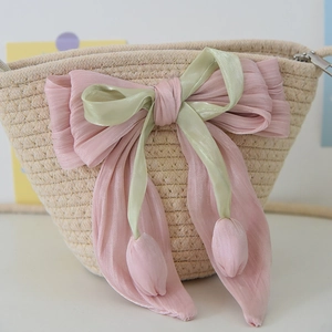 Detailed macro view of woven beach bag featuring a pink organza bow and tulip charms