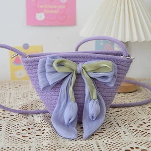 Detail of purple woven bucket bag with a large tulip-shaped satin bow on a lace tablecloth