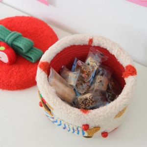 Detail of knitted dog storage basket with a red lid and green bow, filled with snacks