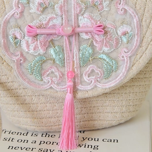 Detail of floral lace embroidery and pink tassel with bead on a woven cotton tote bag