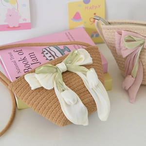 Detail of hand-woven straw crossbody bag featuring large satin bow and tulip pendant charm