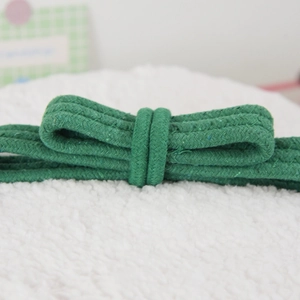 Detail of dark green braided rope in a bow shape on a white textured background