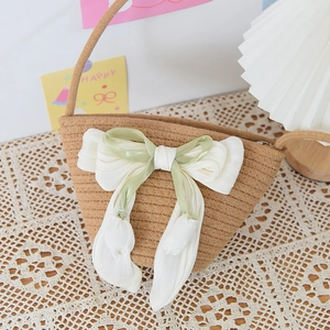 Straw bucket bag with large tulip bow decoration on lace tablecloth background