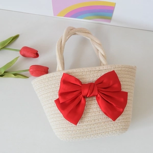 Detail of hand-woven beige straw bag featuring a large decorative red satin bow