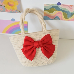 Detail of beige straw handbag featuring a large red satin bow and braided handles