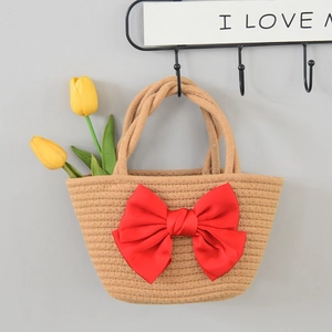 Detail of woven straw handbag featuring a large red satin bow and twin handles