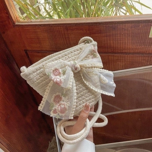 Détail du sac à bandoulière en paille tissée avec nœud en dentelle et broderie florale