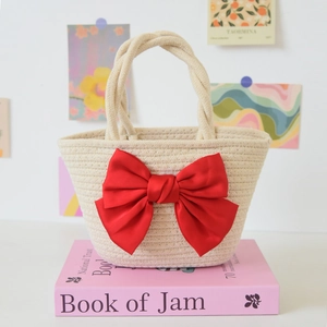 Detail of woven straw handbag featuring a large red satin bow and twisted rope handle