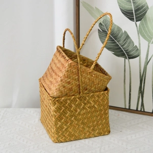 Detail of two square hand-woven seagrass baskets with long handles for home decor