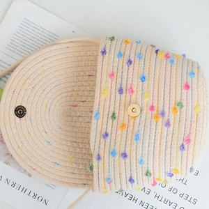Close-up of woven mini beach bag featuring colorful pom-poms and golden magnetic buckle