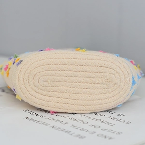 Detailed base of beige woven straw beach bag featuring colorful floral tufted tassels