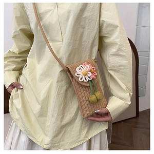 Detail of hand-woven straw phone bag with 3D floral accents for a beach vacation style