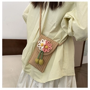 Detail of hand-woven straw crossbody bag with 3D floral accents and green tassels