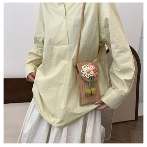 Close-up of a woven straw phone bag featuring a pink daisy floral accent and green charms