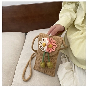 Close-up of hand-woven straw phone bag featuring a 3D floral accent and shoulder strap