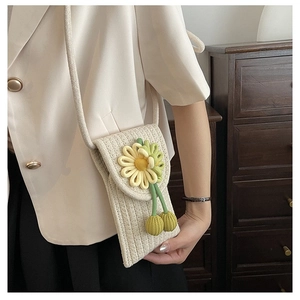 Close-up of cream woven phone bag with yellow crochet flowers and tassels in use