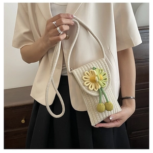 Close-up of woven straw phone bag featuring a yellow daisy and green bead charms
