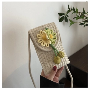 Detail of woven straw phone bag featuring a knitted daisy and long shoulder strap