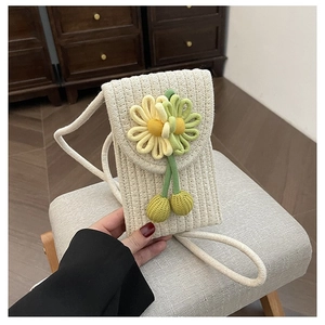 Close-up of handmade woven phone bag with yellow crochet flower and knit ball charms