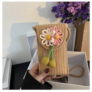 Detailed close-up of woven straw cell phone bag with 3D floral accent in a gift box