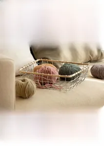 Close-up of iron mesh storage basket with wooden handle and soft knitting yarn balls
