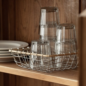 Modern silver wire fruit basket with wooden frame holding glass cups and ceramic plates