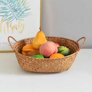 Handwoven seagrass storage basket with double handles holding fresh artificial fruits