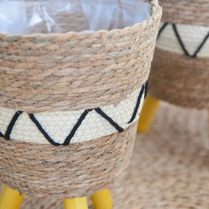 Close-up of Nordic woven seagrass plant basket with embroidery and wooden tripod legs