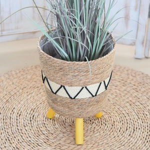 Detail of Nordic woven straw planter basket featuring geometric patterns and wooden legs