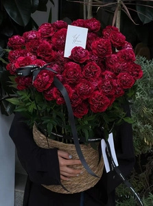 Close-up of red carnations in a round brown woven basket with elegant ribbons