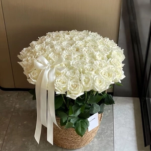 Close-up of elegant white roses in a round woven gift basket with a silk ribbon bow