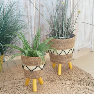 Detail of woven straw plant pots with black wave pattern and wooden tripod legs