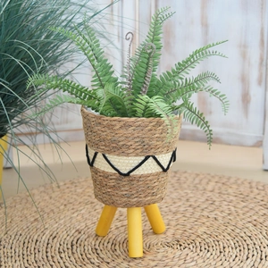 Detail of hand-woven seagrass planter with black wave pattern and wooden tripod legs